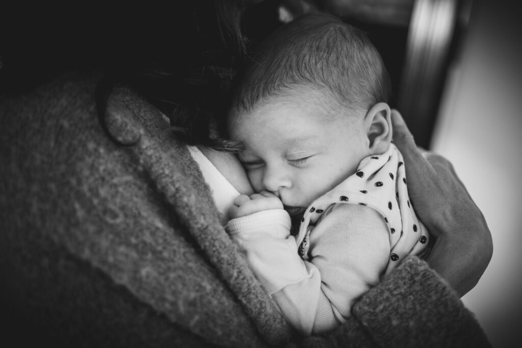 Mother snuggling her newborn baby girl close in this black & white image. 