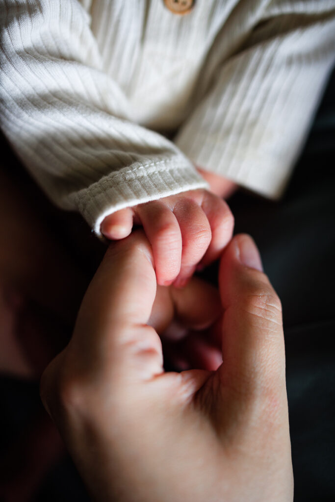 Moody image of a newborn baby holding his mother's hand.