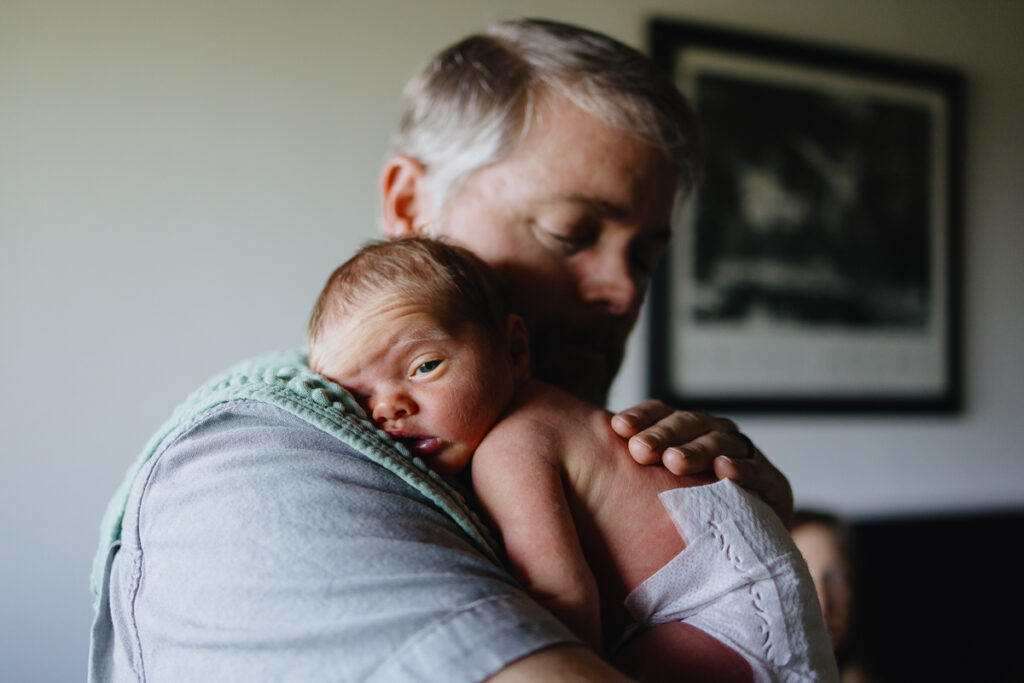Newborn baby wearing only a diaper dozes off on his father's shoulder. 