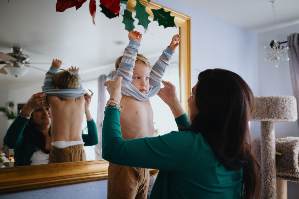 A mom removes her toddler's shirt. 
