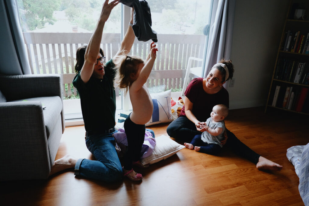 Her removes his toddler's shirt while mom and baby sister happily watch in the background. 