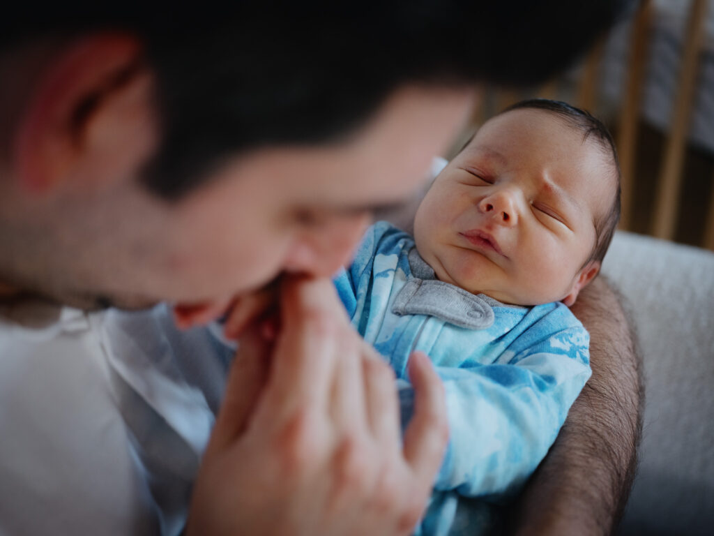 A newborn baby frowns as his dad kisses his hand.