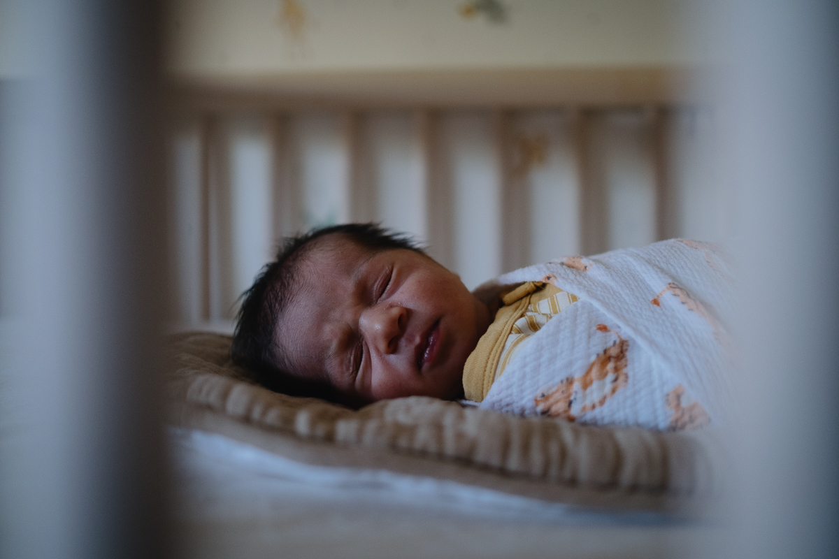 Newborn baby wearing muted mustard tones asleep in his crib.