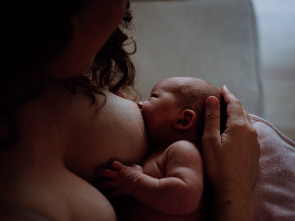 Dimly lit image of a newborn baby breastfeeding while doing skin-to-skin with mom.
