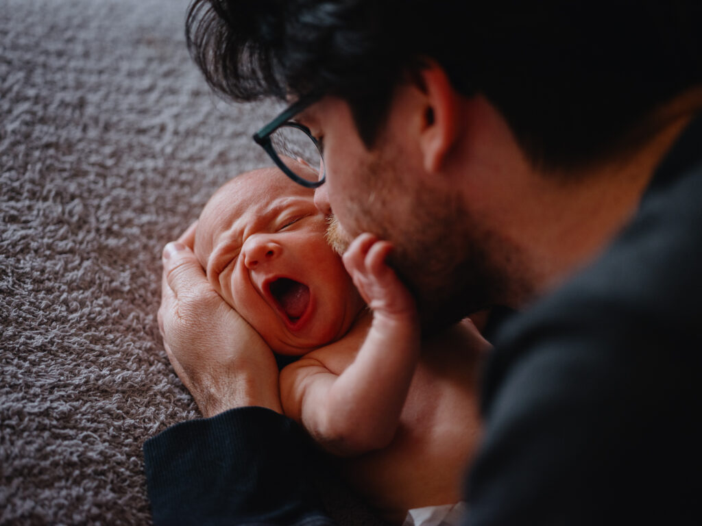 A newborn baby is playfully snuggled by his father.