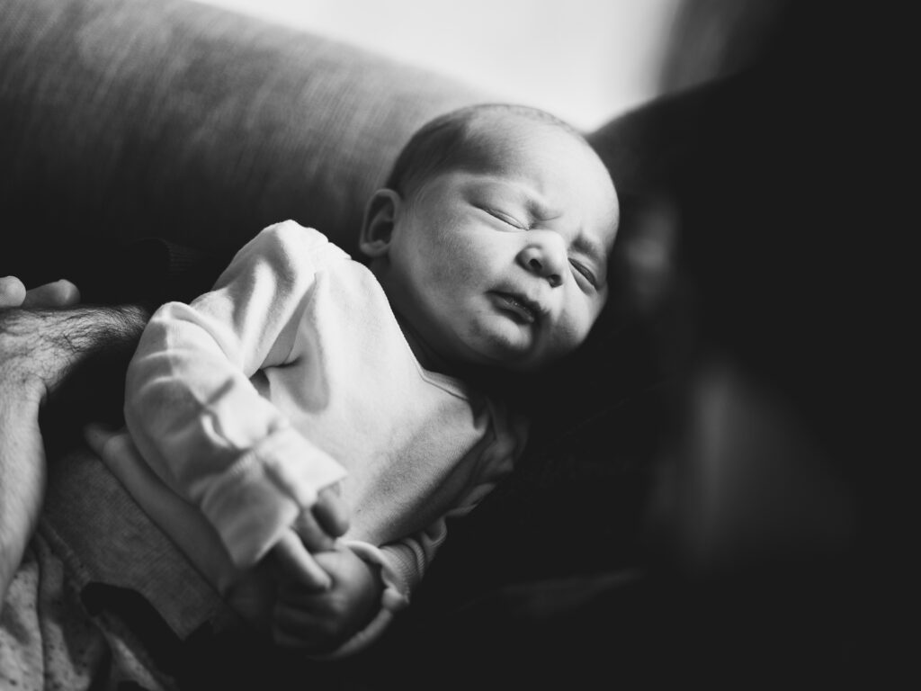 Black & white portrait of a newborn baby sleeping in her parent's arms. 