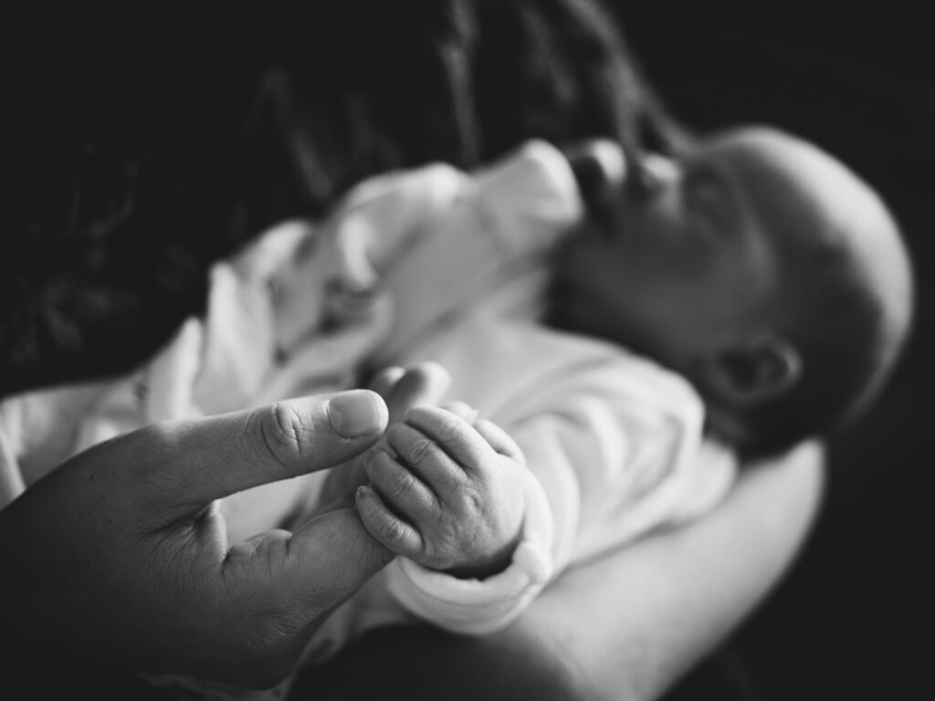 Newborn baby's hand holds her parent's hand in this black & white image. 