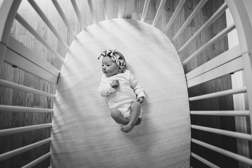 Black & white overhead image of a newborn baby lying in her crib. 