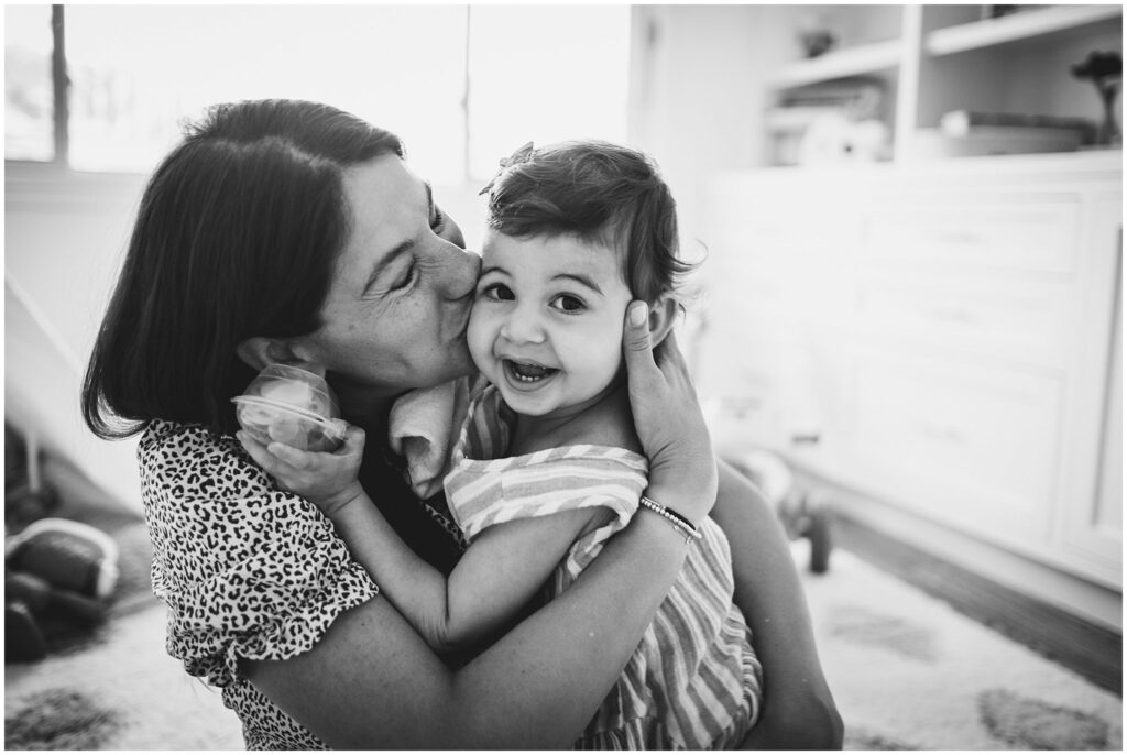 Black & white image of a mother smooching her toddler daughter, who is smiling and looking towards the camera, an example of what to wear that also works in black & white.