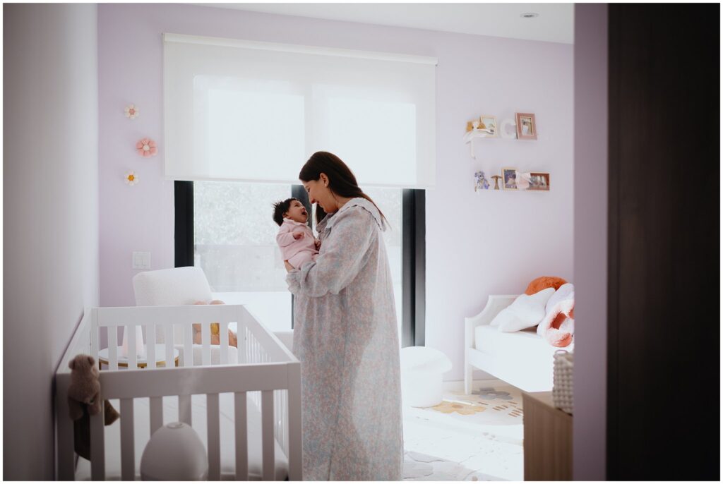 Wide shot of a mom standing in her baby's purple nursery, cuddling her baby. 