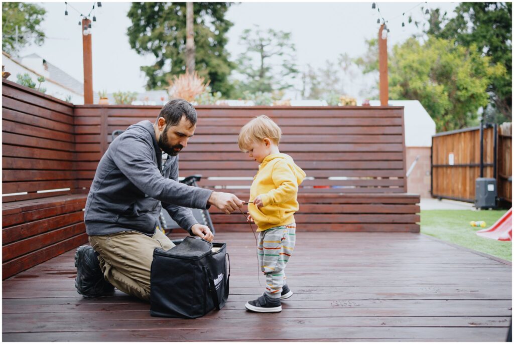 A wide image outside of a dad and his toddler son setting up a toy together. 