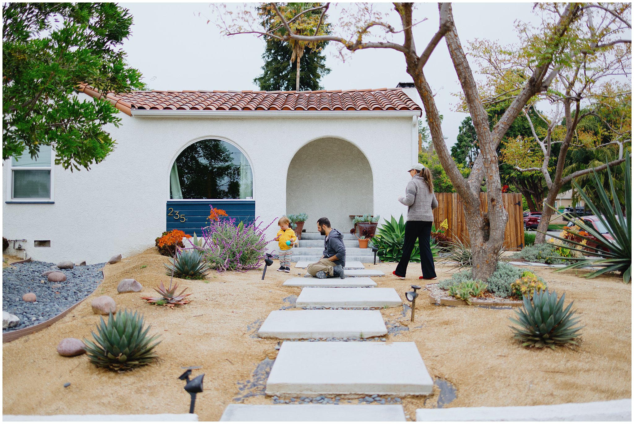 Wide shot of the outside of a house showing adoptive parents playing with their child.
