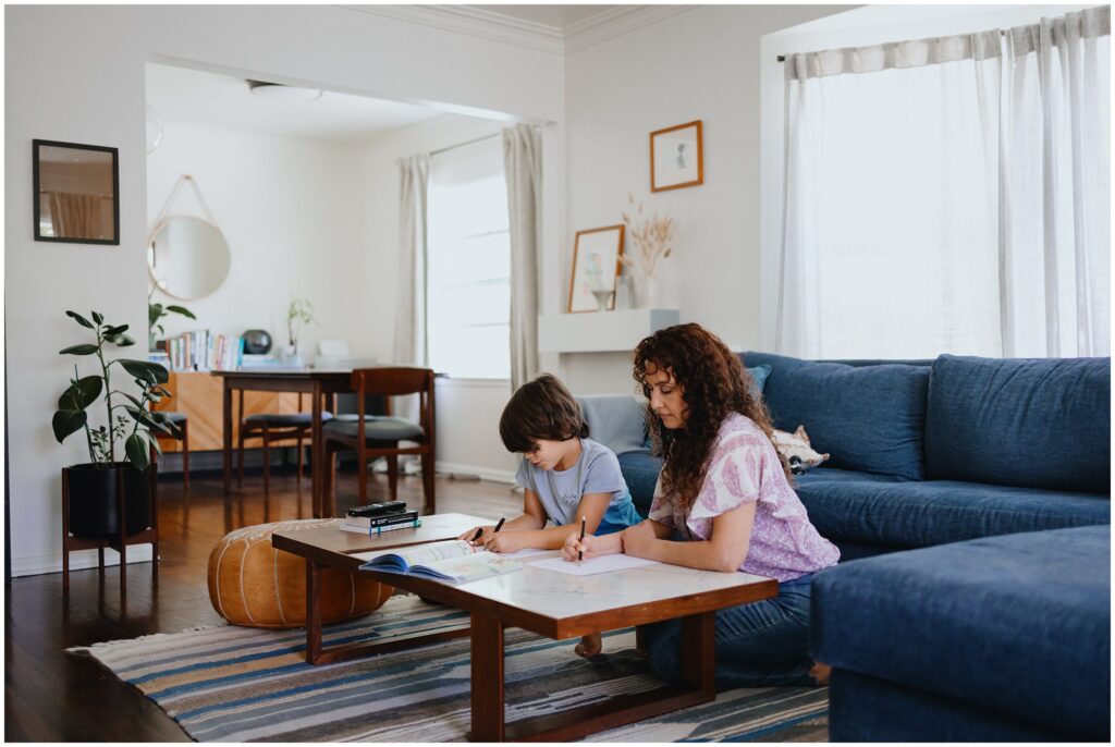 Wide-angle image of divorced mom and son drawing together over their coffee table in the living room. 