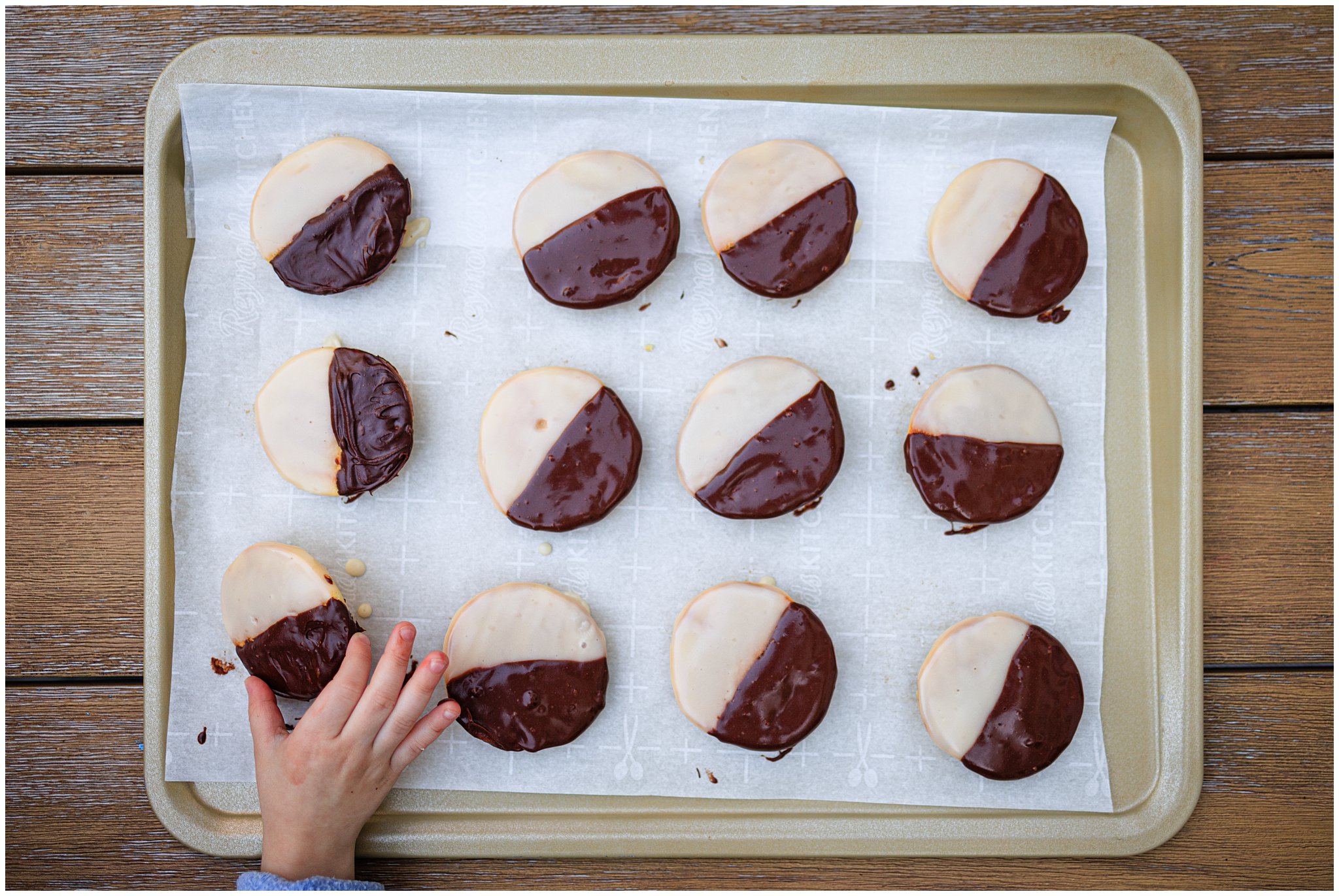 A tray of black & white cookies with a child's hand picking up one of the cookies.