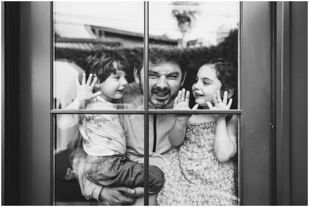 Black & white photo of a father and his two young kids taken during an at-home family photo session. 