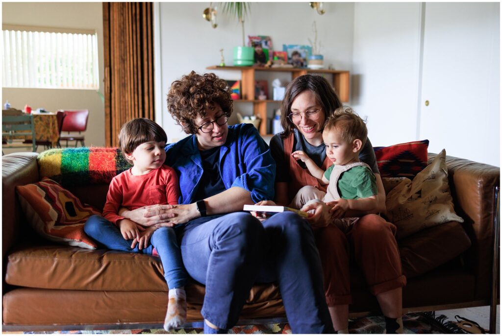 Two moms and their children reading on the couch during an at-home family photo session. 