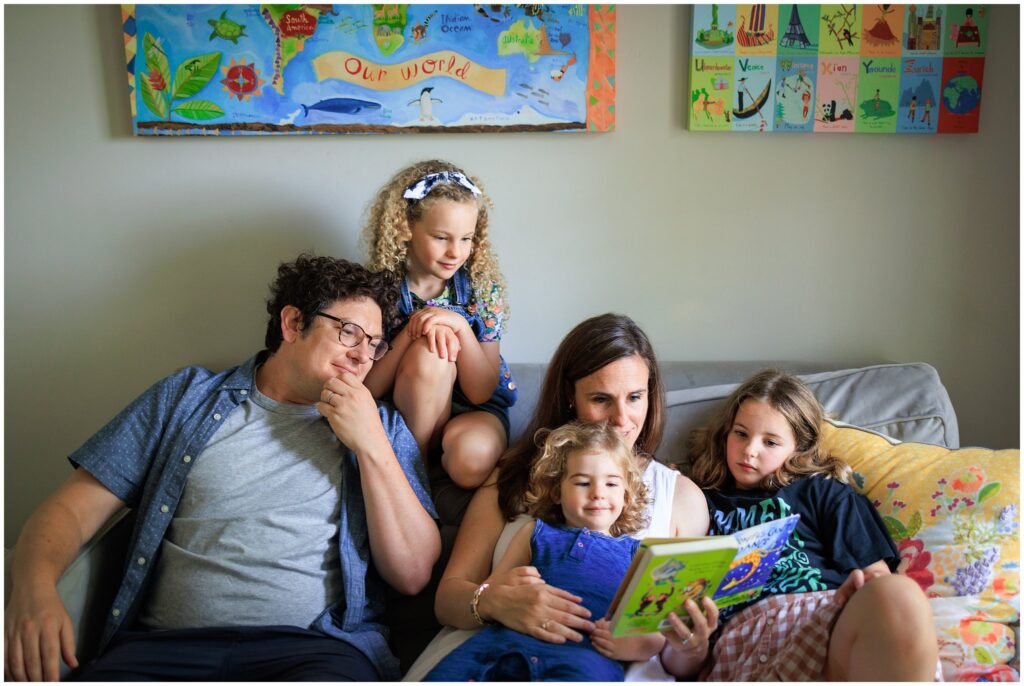 Parents reading books with their three children on the couch during an at-home family photo session. 