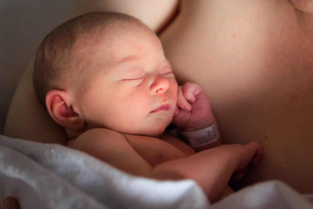 Newborn baby lies on mom's chest during their hospital newborn photos.